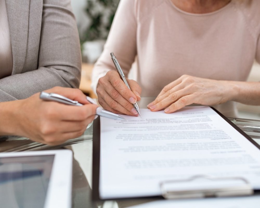 One of two businesswomen with pens going to put signature on page of contract Two businesswomen with pens pointing at contract while one of them going to put signature after reading the document